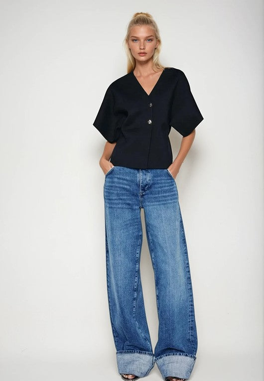 Woman wearing a black top metal button cardigan and blue jeans on a white background